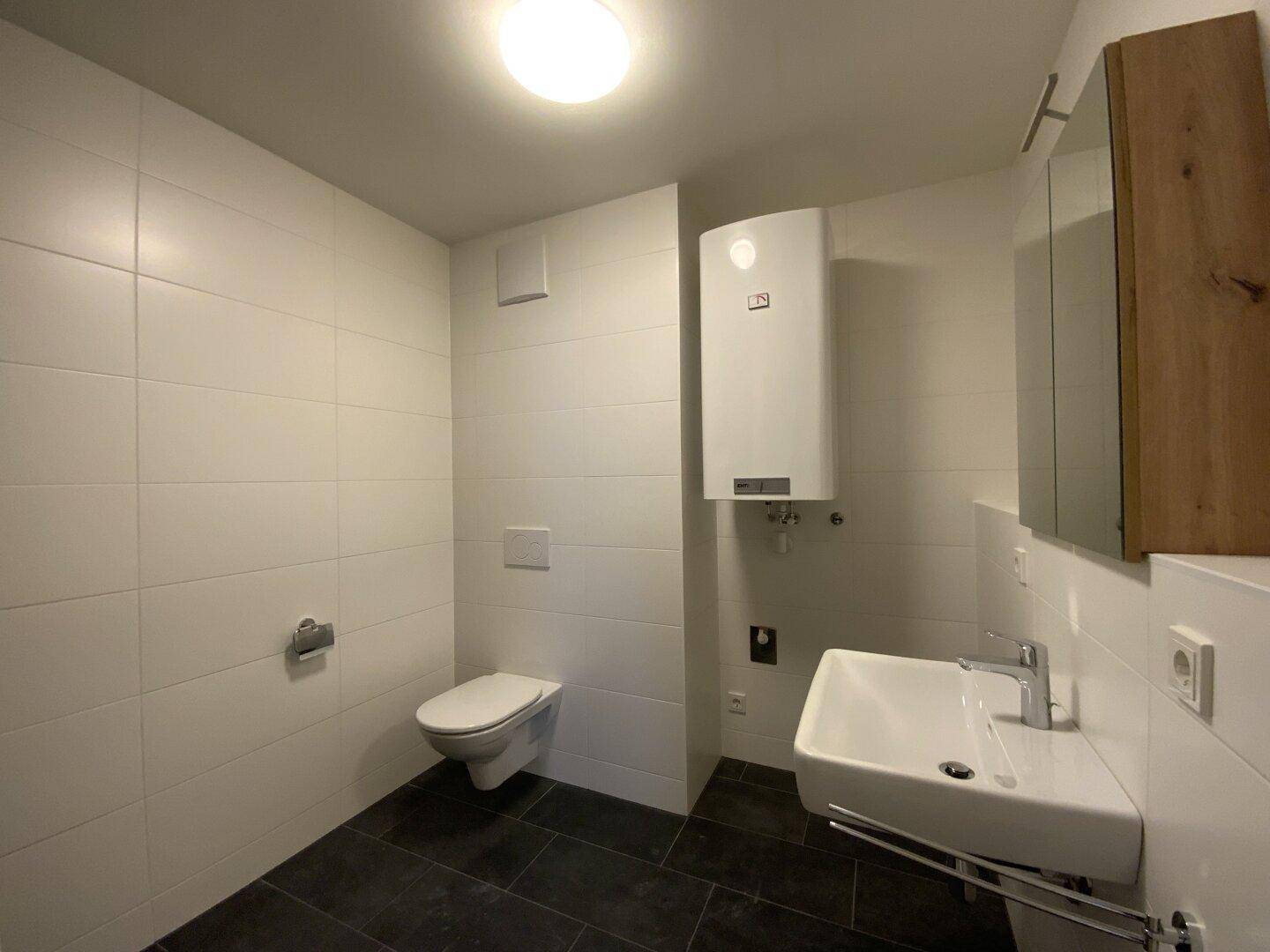 Modernes Badezimmer mit weißen Fliesen, wandhängendem WC und Waschbecken.