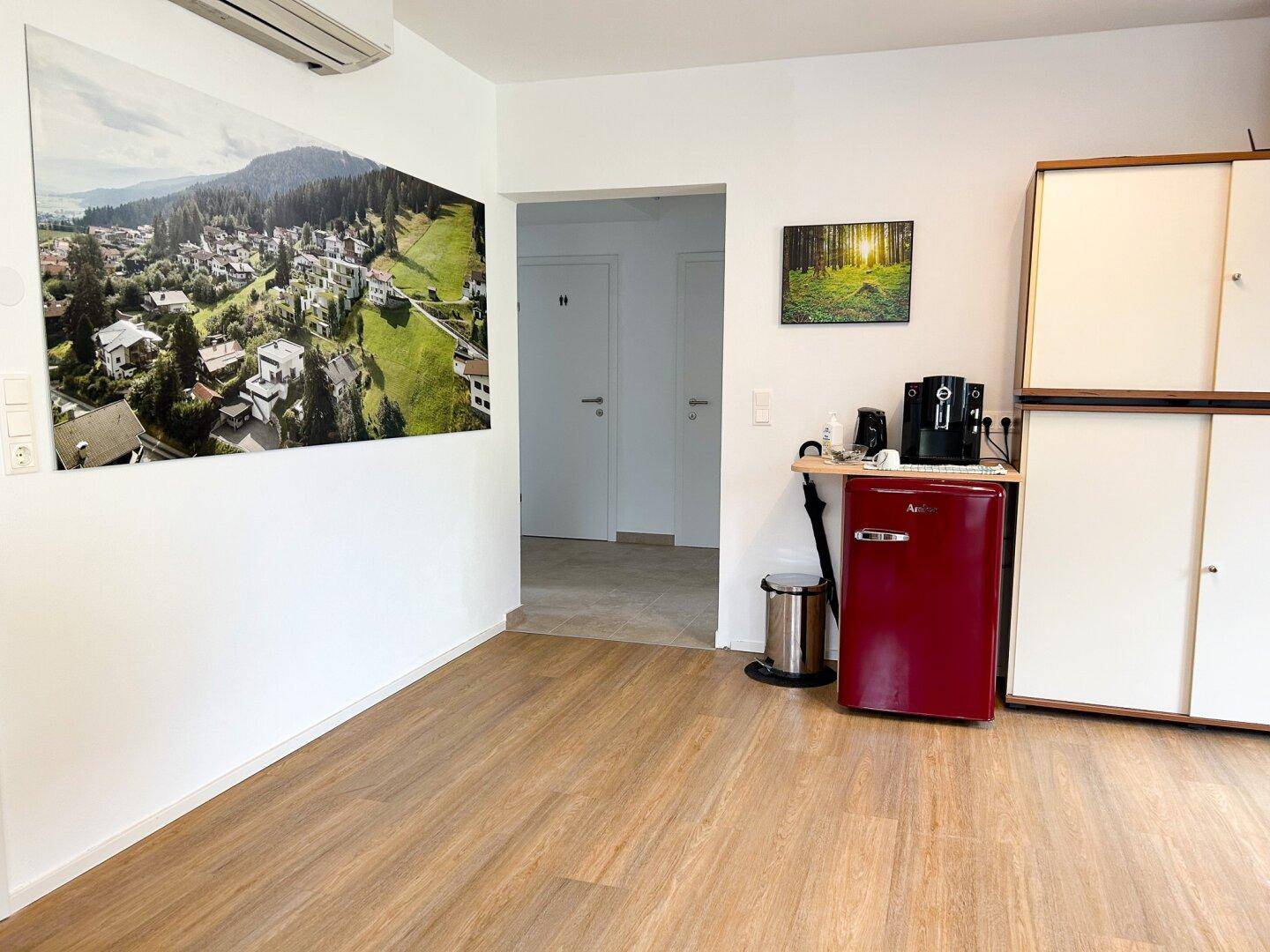 Bereich mit kleinem Kühlschrank, Kaffeemaschine und Wandbild, ideal als Pausen- oder Wartezone.