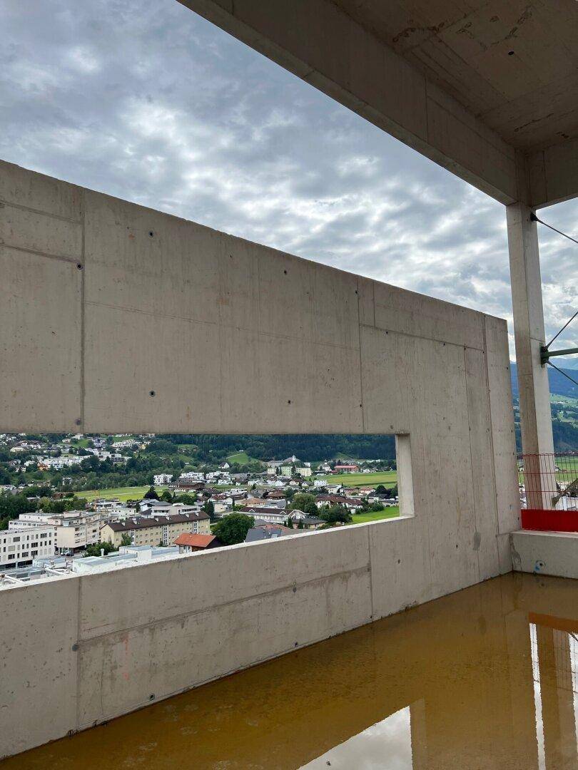Aussicht von einer Baustelle durch eine Betonöffnung auf die Stadt und grüne Hügel.