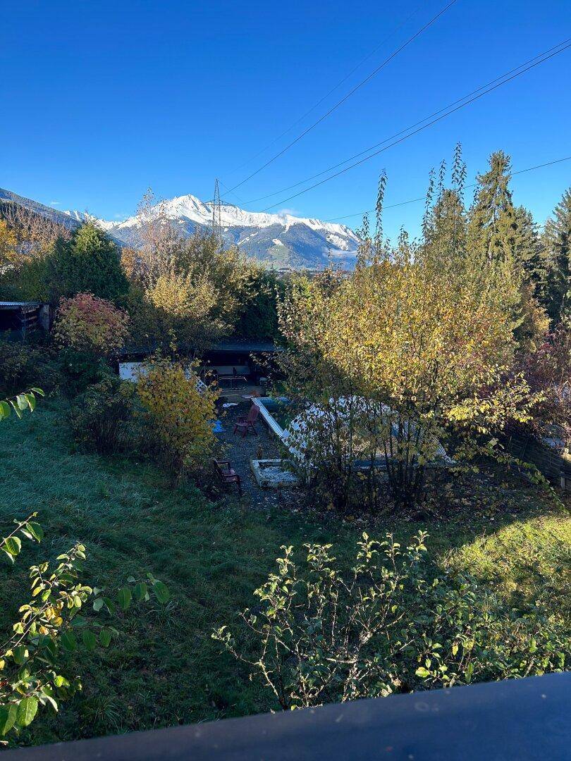 Herbstlicher Gartenbereich mit bunten Bäumen und weitem Blick auf die schneebedeckten Berge.