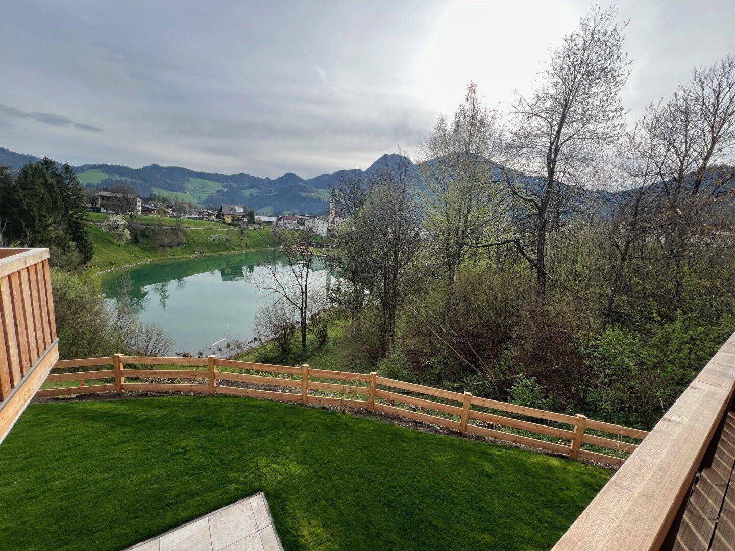 Blick von der Terrasse auf einen gepflegten Rasen, einen See und die malerische Bergkulisse.