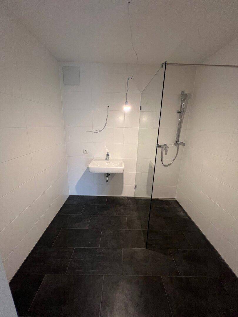 Modernes Badezimmer mit weißen Fliesen, dunklem Boden und einer begehbaren Dusche mit Glaswand.