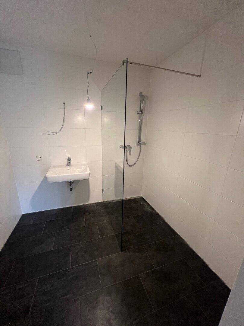 Helles Badezimmer mit weißen Wandfliesen, dunklem Boden und einer modernen, begehbaren Dusche.