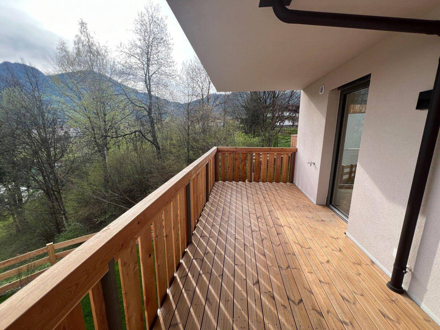 Heller Holzbalkon mit Blick auf grüne Bäume und die beeindruckende Berglandschaft.