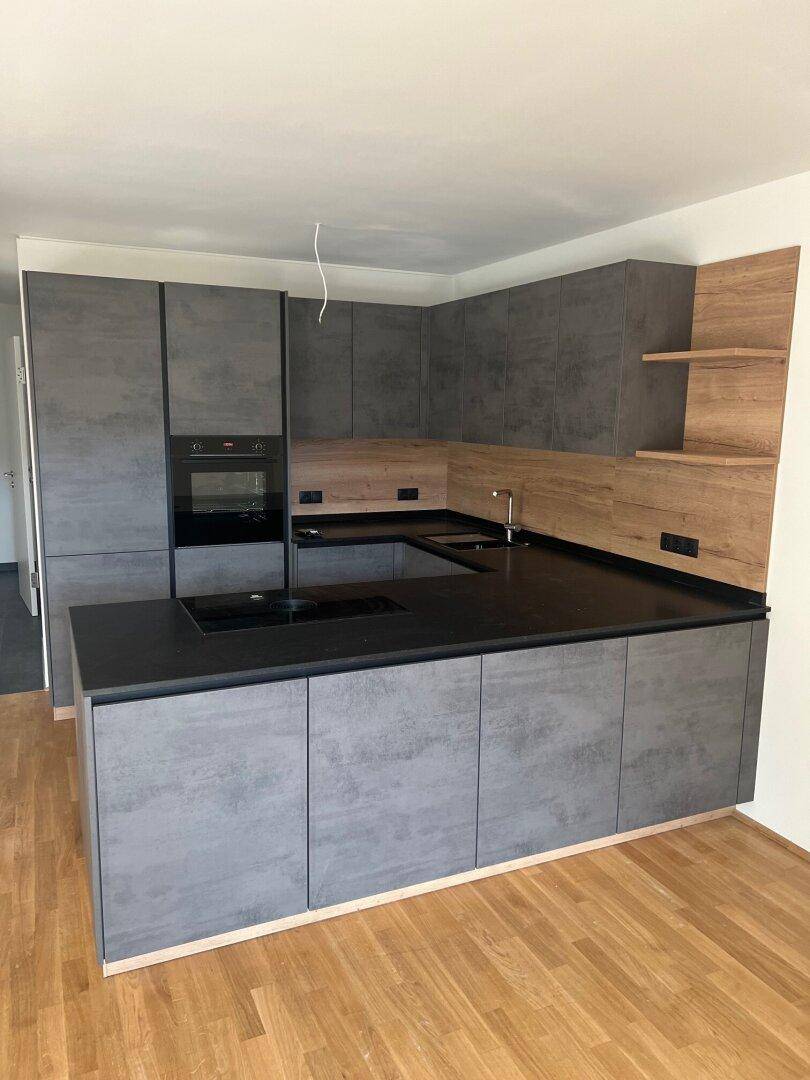 Moderne Einbauküche mit grauen Fronten, dunkler Arbeitsplatte und integriertem Kochfeld auf der Insel.