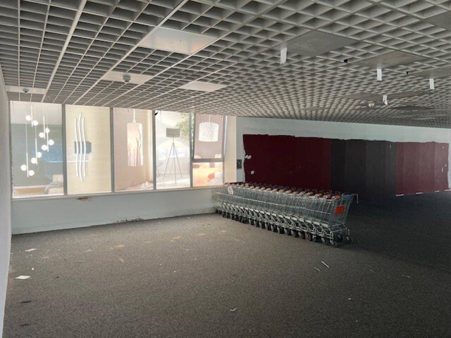 Leerstehender Gewerberaum mit Teppichboden und Rasterdecke, Einkaufswagen im Hintergrund.