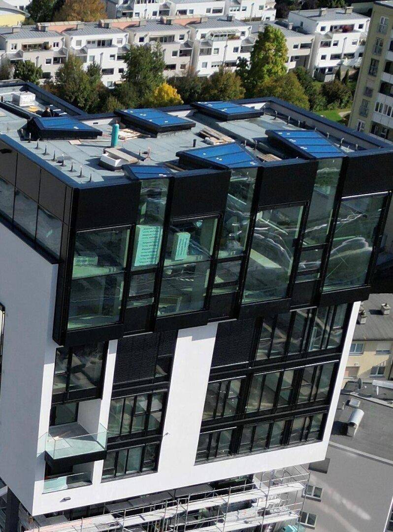 Detailansicht der oberen Etagen eines modernen Gebäudes mit großen Glasflächen und Dachfenstern.