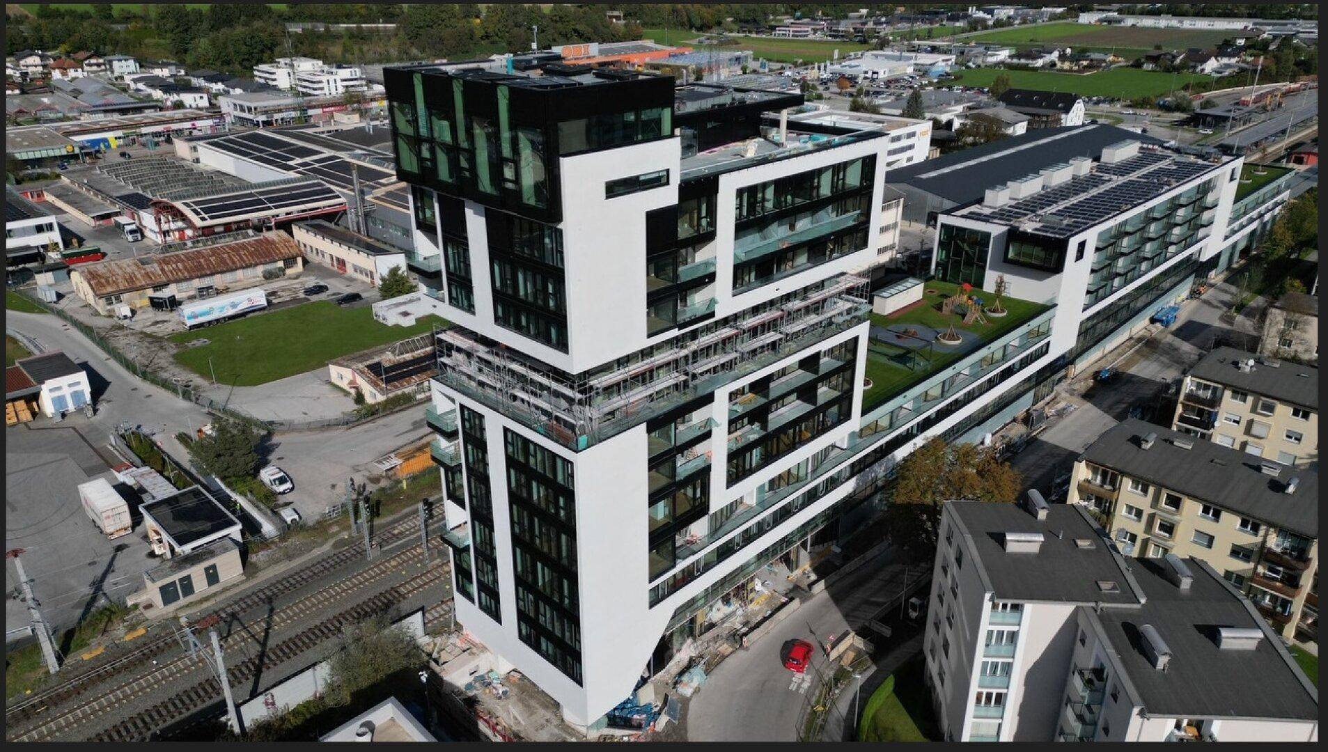 Luftaufnahme eines gestuften modernen Gebäudes mit zahlreichen Balkonen und Glasfronten in urbaner Lage.