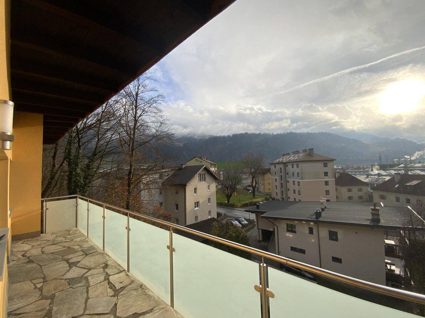 Balkon mit Steinplattenboden, Glasgeländer und weitem Blick auf die Landschaft.