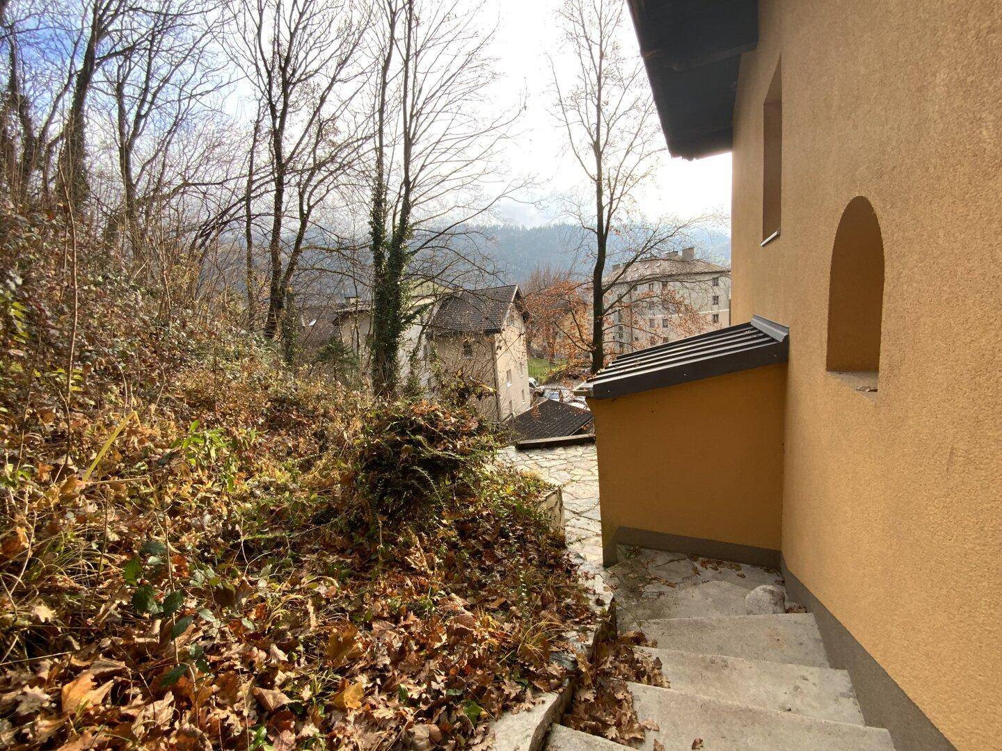 Hanglage mit bewachsenem Pfad und Blick auf die darunter liegenden Gebäude.