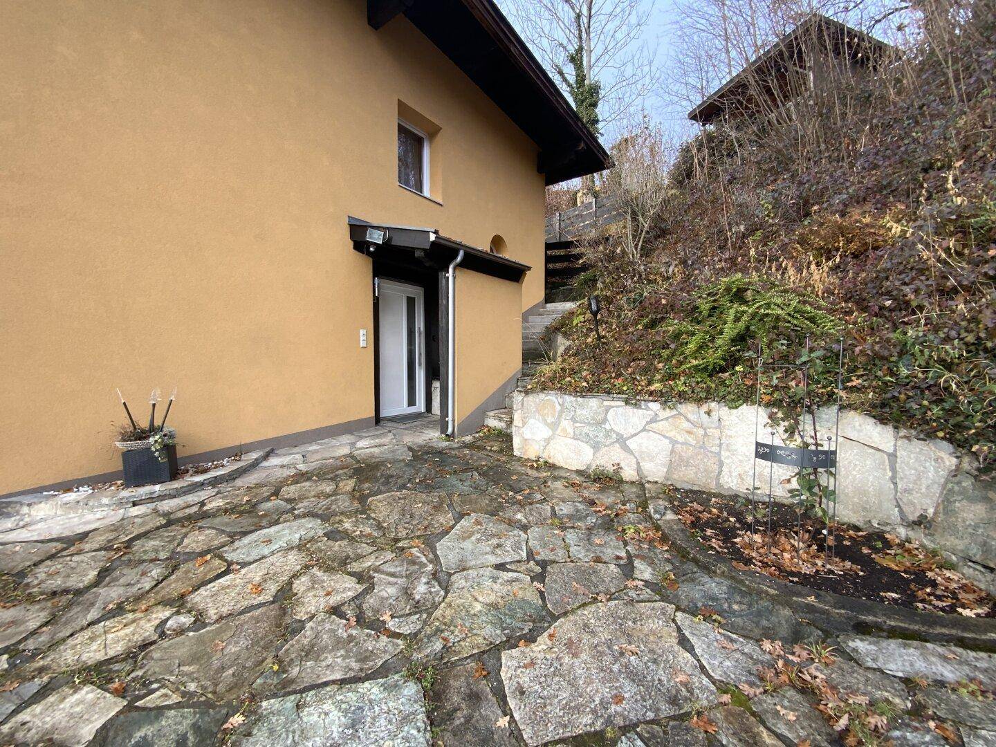 Eingangsbereich des Hauses mit Steinplatten und umgebender Bepflanzung.