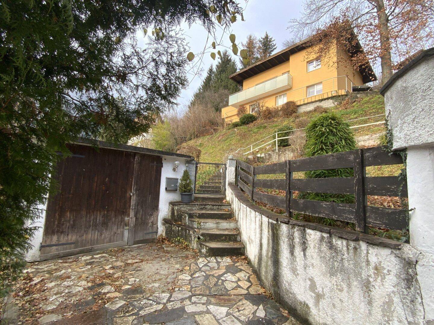 Haus auf Hanglage mit Garage, Steintreppe und umgebender Vegetation.
