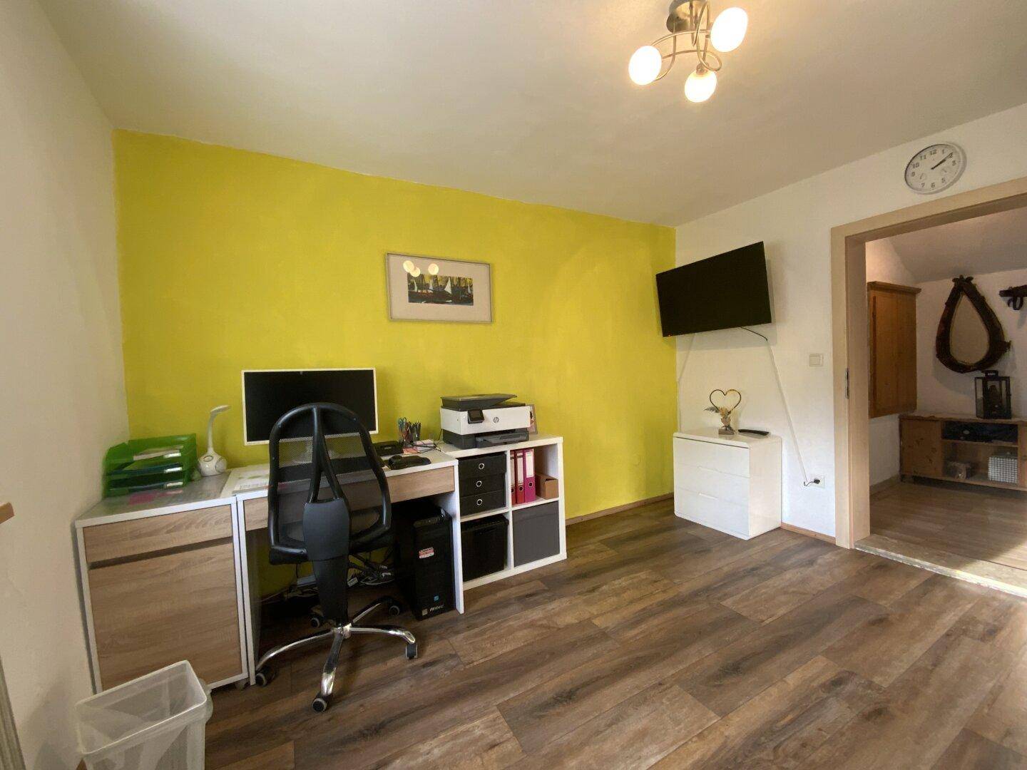 Arbeitszimmer mit gelber Akzentwand, Holzfußboden und Schreibtisch.
