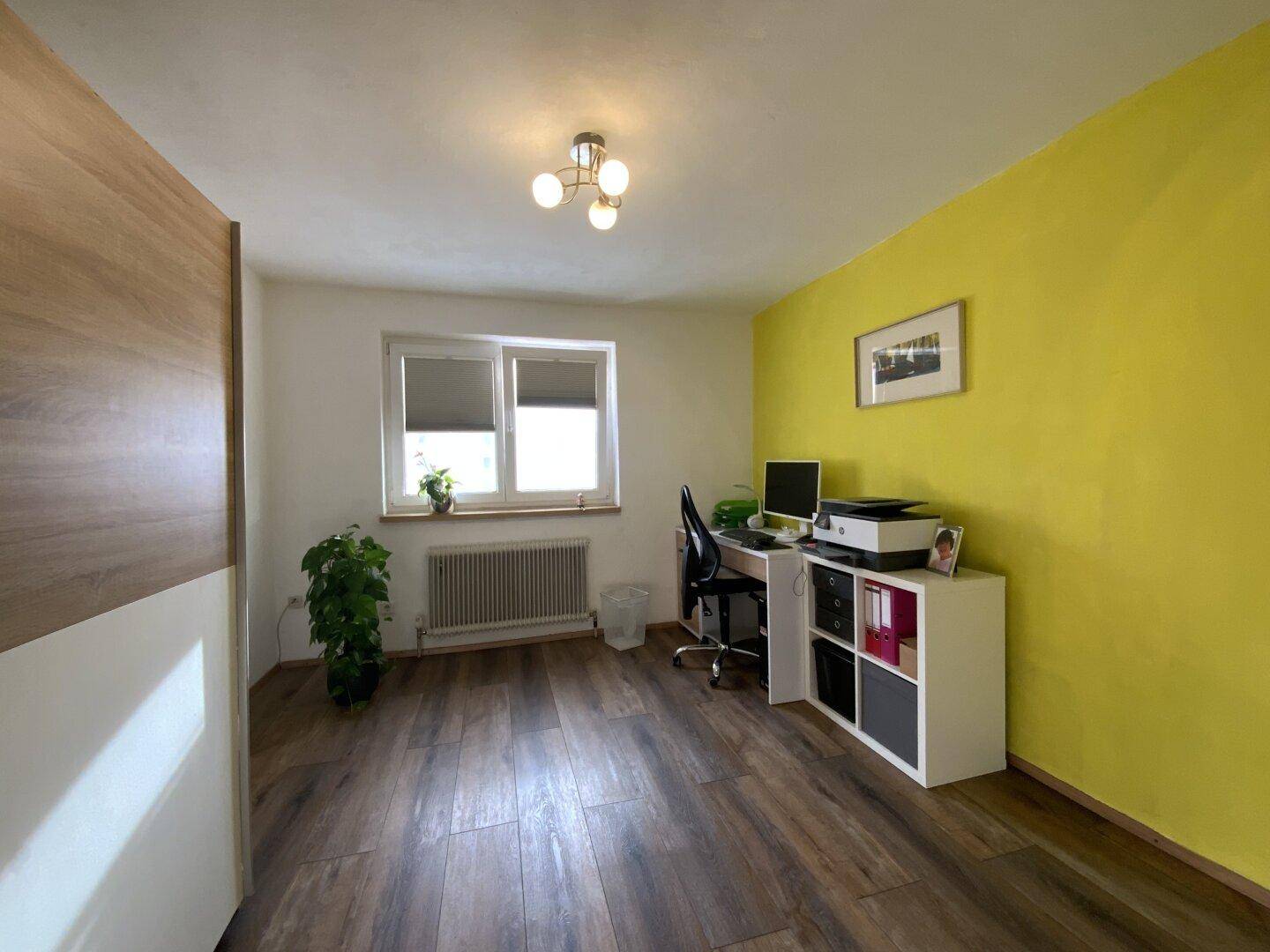Helles Arbeitszimmer mit Fenster, gelber Wand und Laminatboden.