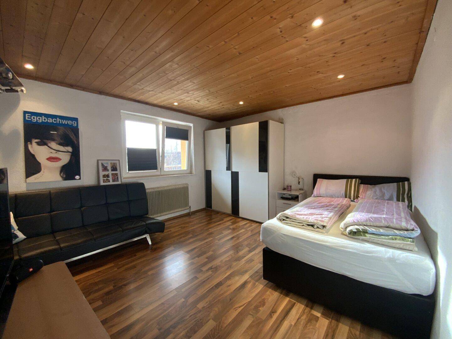 Schlafzimmer mit Holzbalkendecke, Laminatboden und Doppelbett.