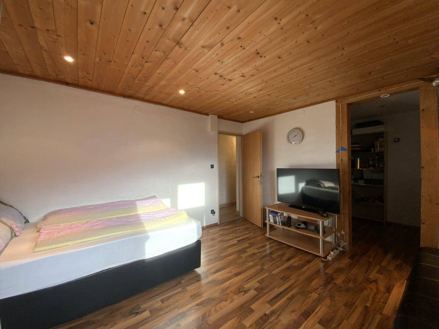 Gemütliches Schlafzimmer mit Holzbalkendecke, Laminatboden und TV-Bereich.