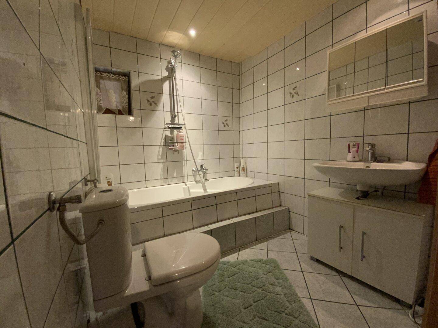 Badezimmer mit Badewanne, WC und weißen Fliesen an Wänden und Boden.