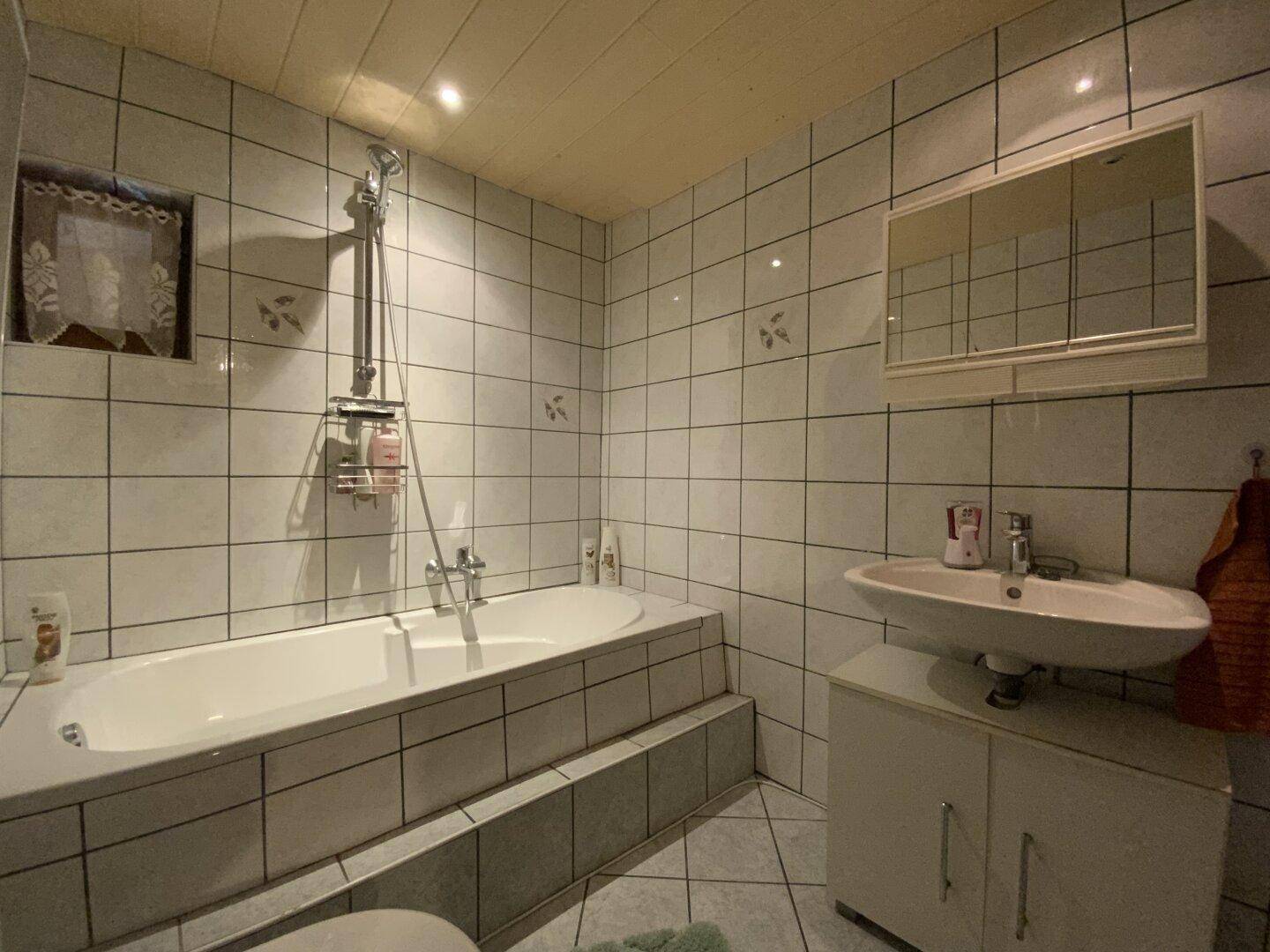 Helles Badezimmer mit Badewanne, Waschbecken und weißen Fliesen.