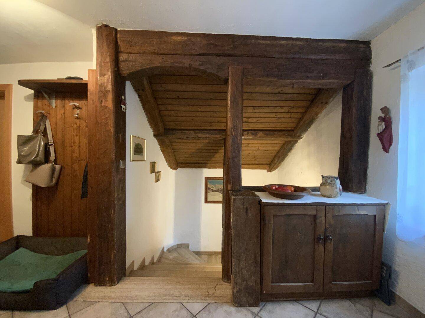 Flurbereich mit sichtbaren Holzbalken, rustikalem Schrank und Zugang zur Treppe.