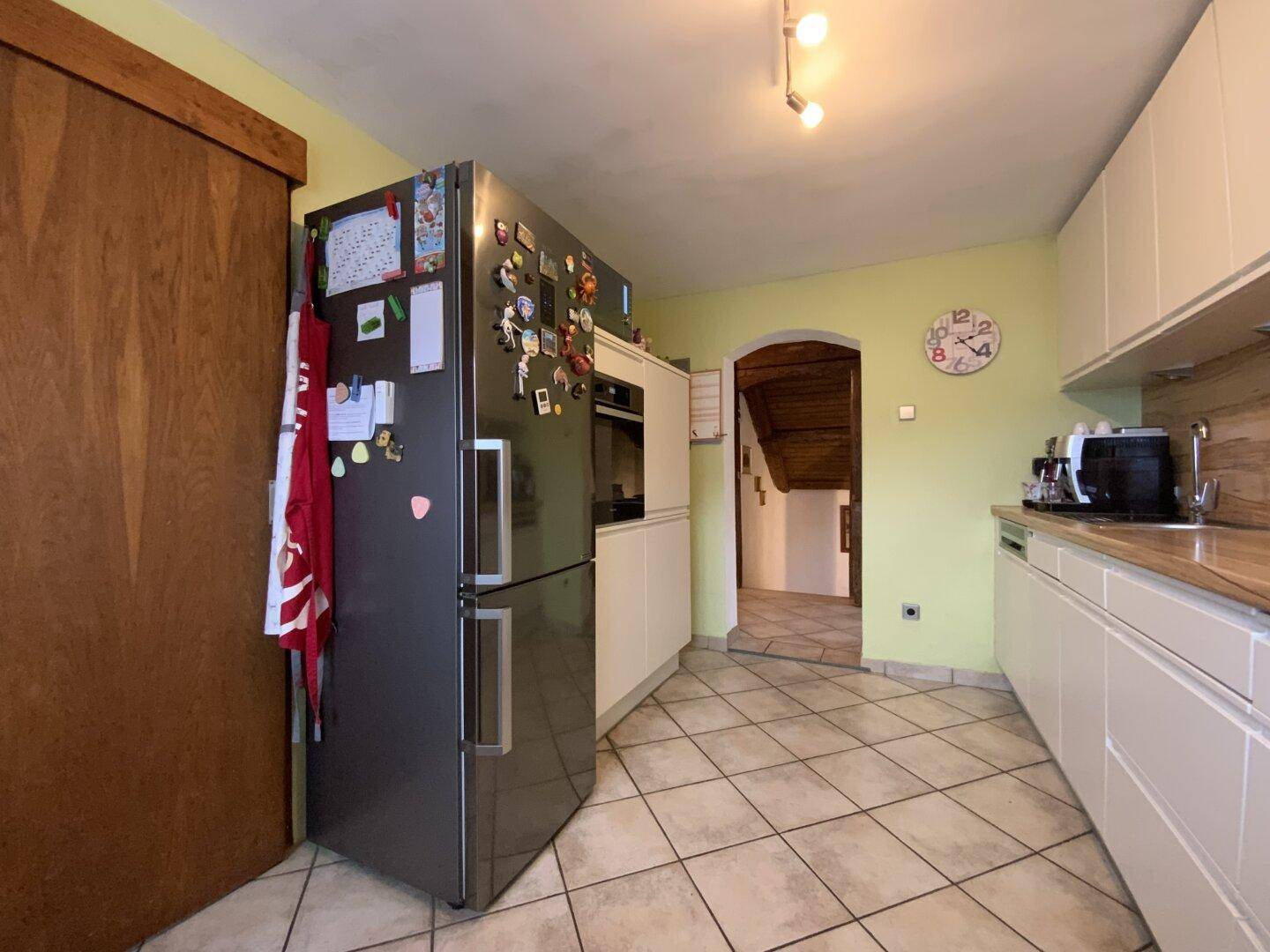Küche mit großem Kühlschrank, Fliesenboden und Zugang zum Flur durch einen Bogen.