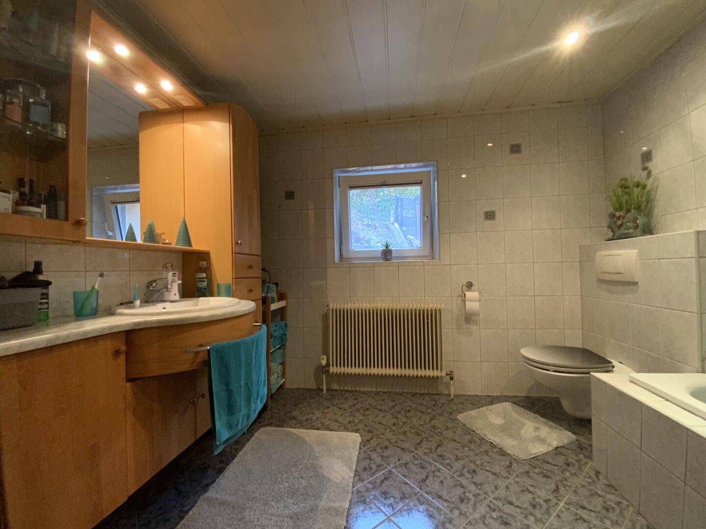 Badezimmer mit Badewanne, WC, Holzwaschtisch und Fenster.