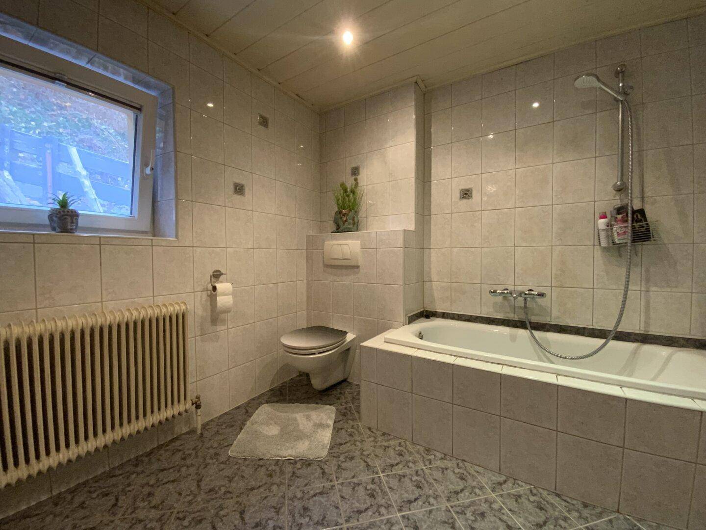 Helles Badezimmer mit Badewanne, WC und Fliesen an Wänden und Boden.