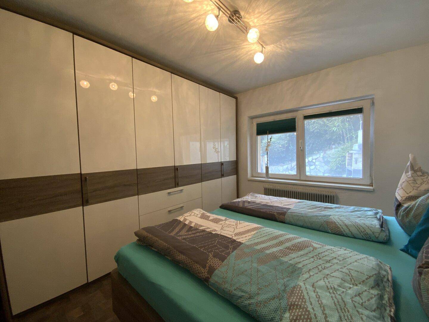 Schlafzimmer mit großem Einbauschrank, Doppelbett und Fenster.