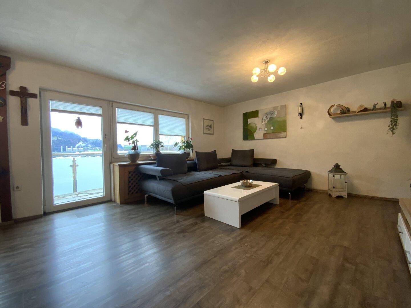 Wohnzimmer mit großem Ecksofa, Laminatboden und Balkonzugang.