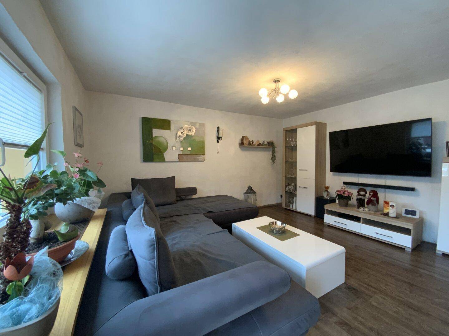 Geräumiges Wohnzimmer mit modernem Sofa, TV und Blick nach draußen.