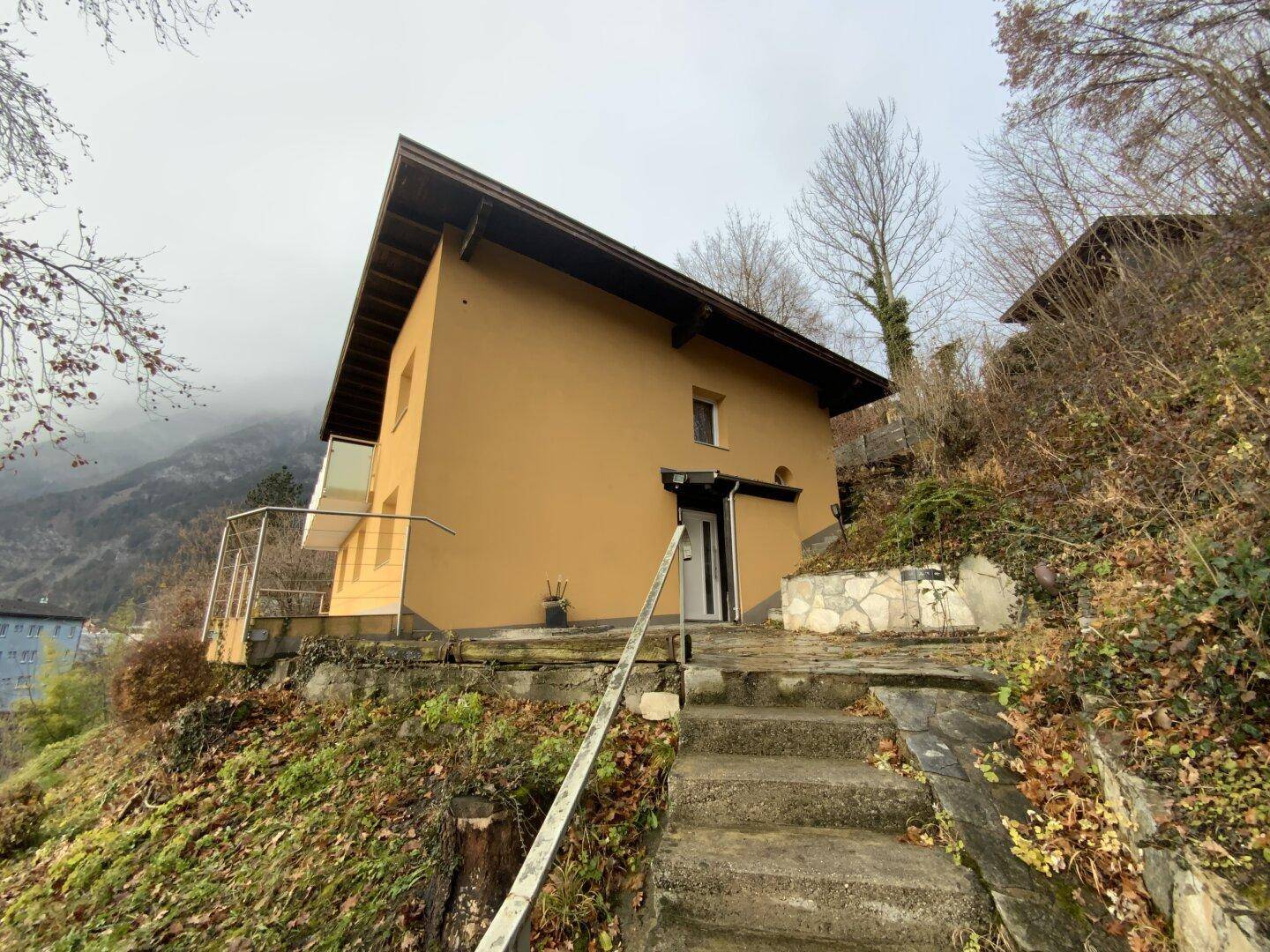 Hausfassade auf Hanglage mit Eingangsbereich und Balkon.