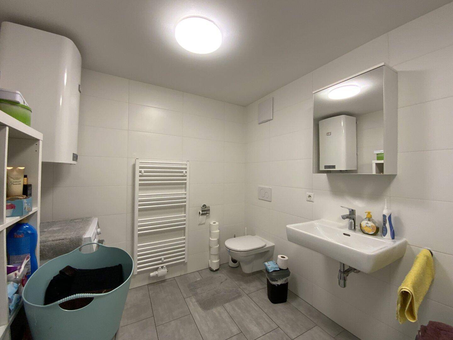 Funktionales Badezimmer mit WC, Waschbecken, beheiztem Handtuchhalter und Waschmaschine.