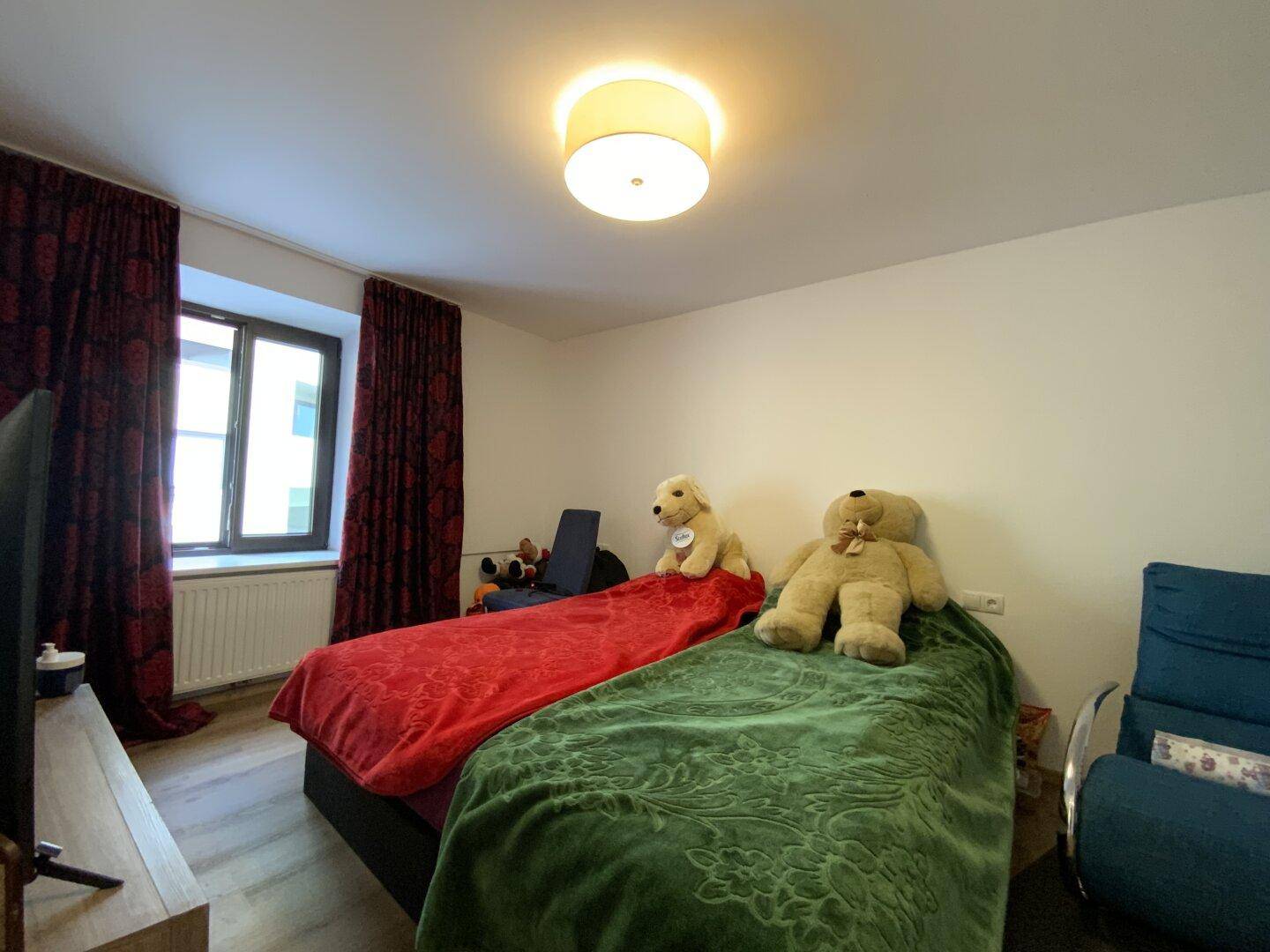 Gemütliches Schlafzimmer mit zwei Betten, Fernseher und Fenster mit blickdichten Vorhängen.