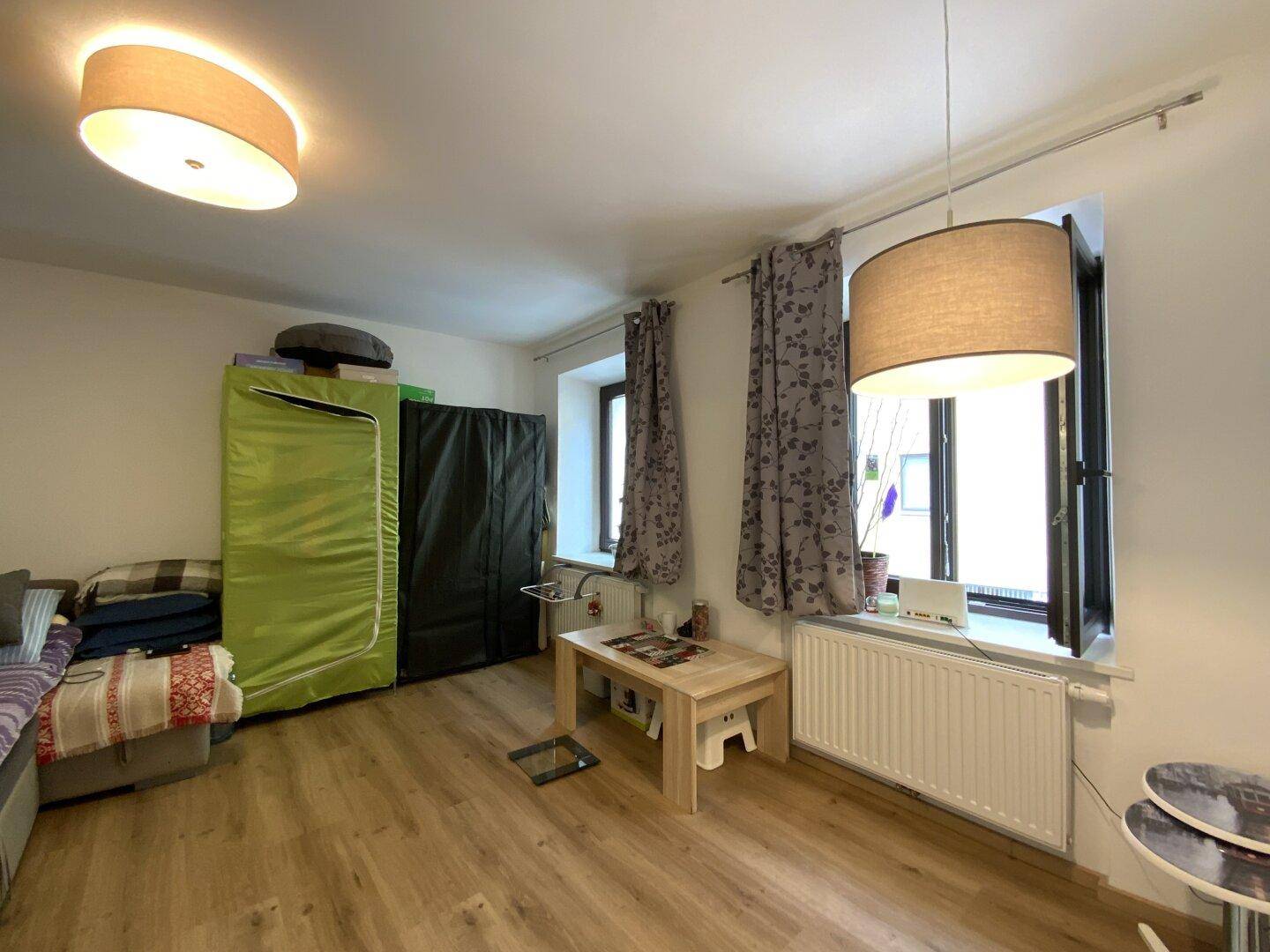 Wohnzimmer mit Laminatboden, kleinem Couchtisch und Fenster, das Tageslicht hereinlässt.