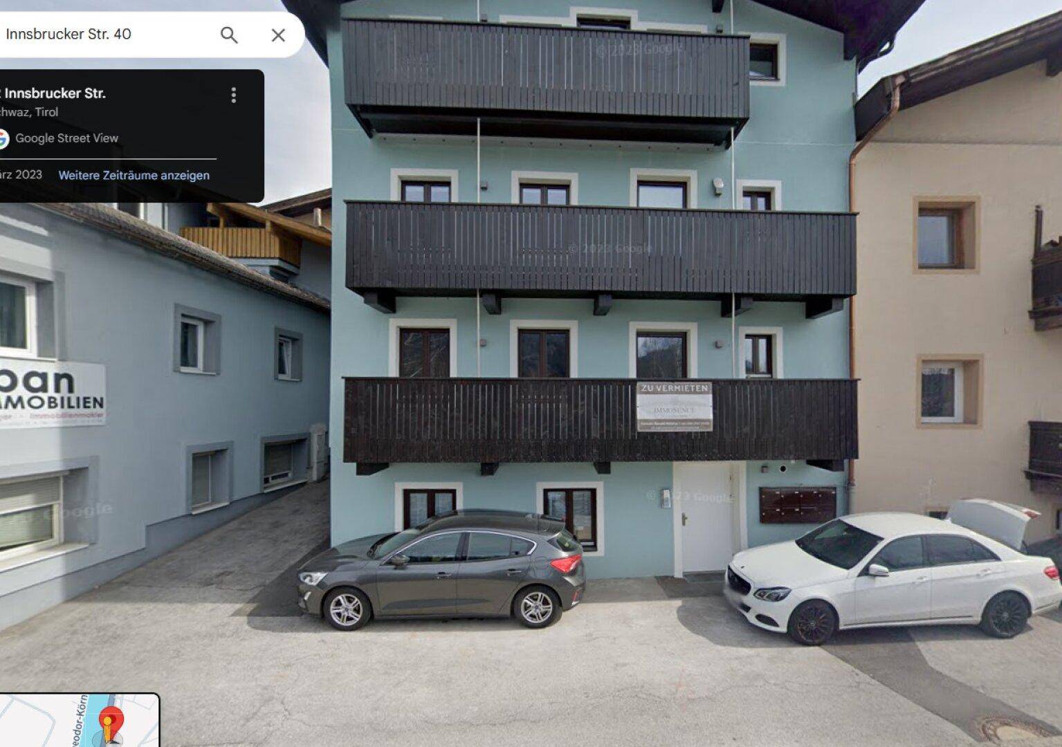 Mehrstöckiges Gebäude mit Balkonen und geparkten Autos auf der Straße.