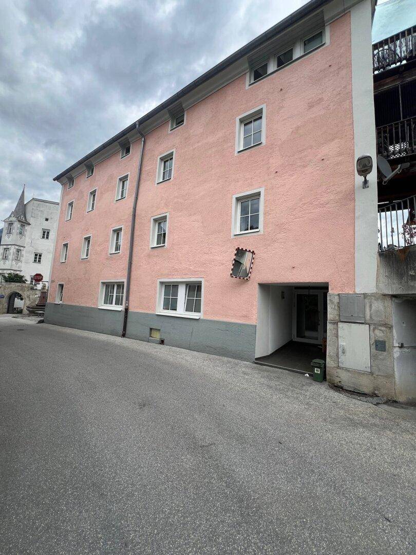 Seitenansicht des Gebäudes mit rosafarbener Fassade und einem überdachten Eingangsbereich oder einer Garagenzufahrt.