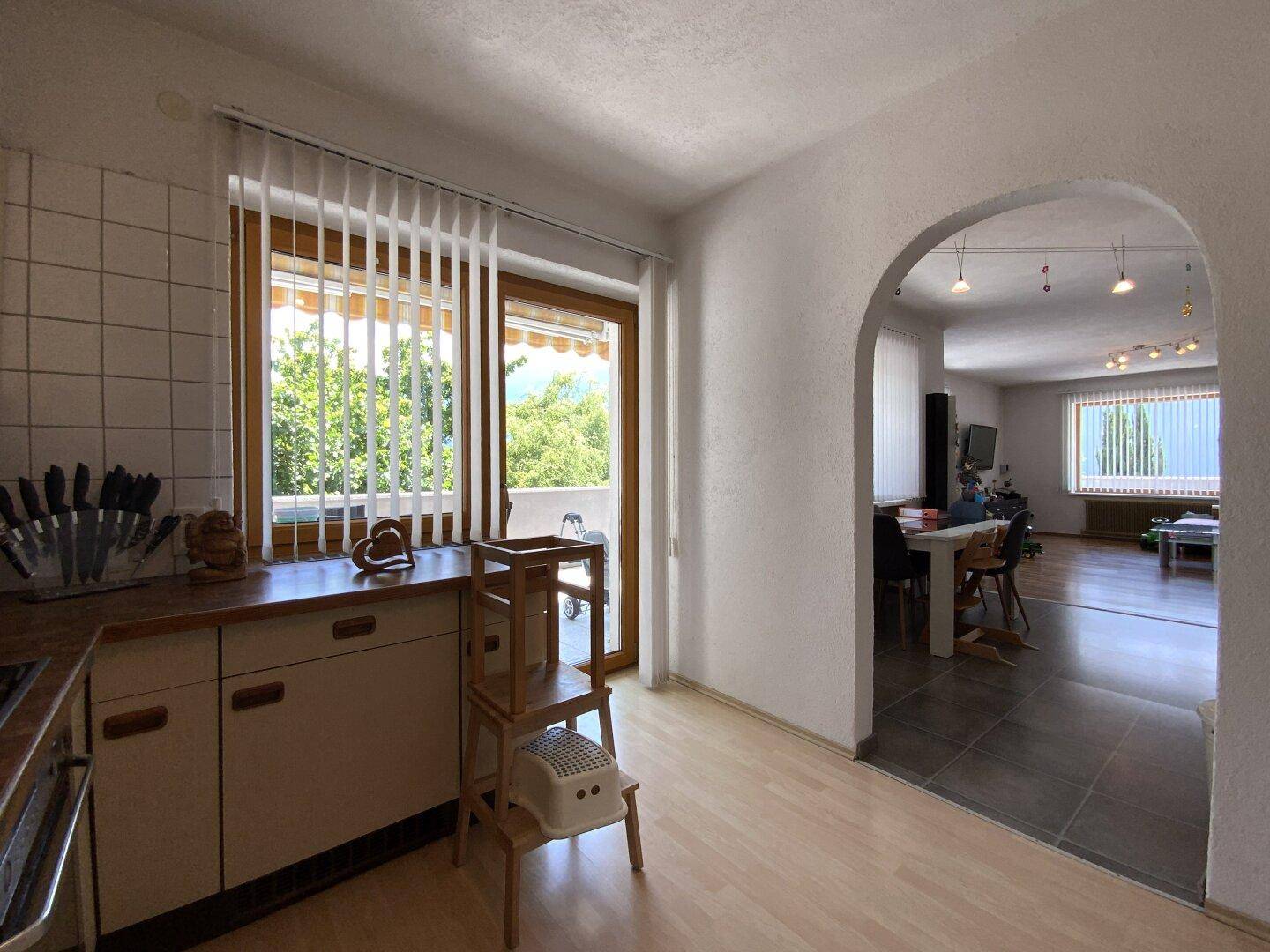 Helle Küche mit Fenster und offenem Durchgang zum Essbereich und Wohnzimmer.