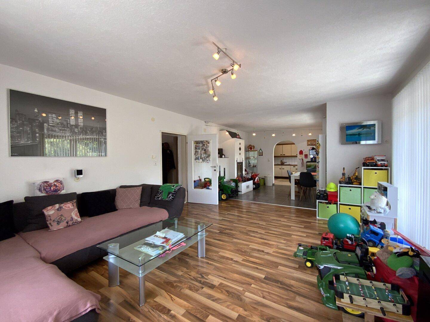 Geräumiger Wohnbereich mit Laminatboden, Sofa und offenem Übergang zum Essbereich.