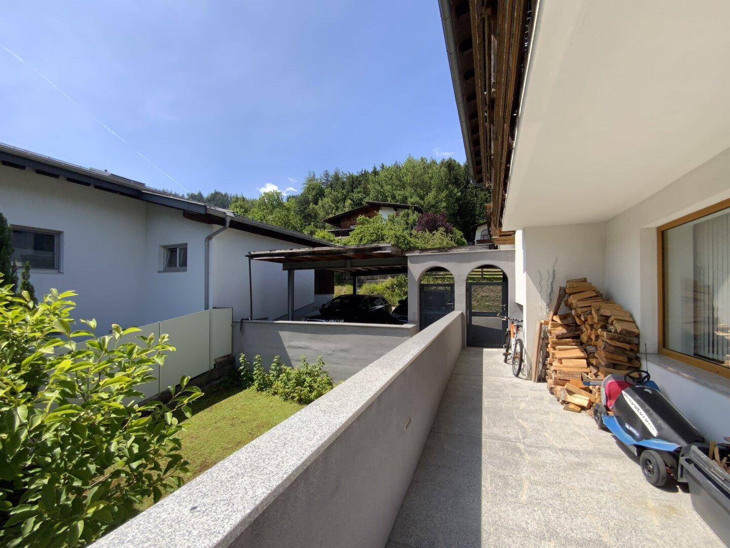 Langer Balkon mit Holzstapel und Blick auf den Carport und die Umgebung.