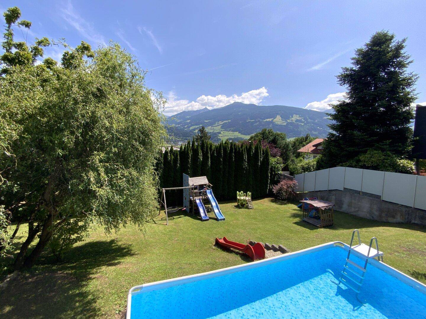 Weitläufiger Garten mit Aufstellpool, Kinderspielplatz und Blick auf die Berge.