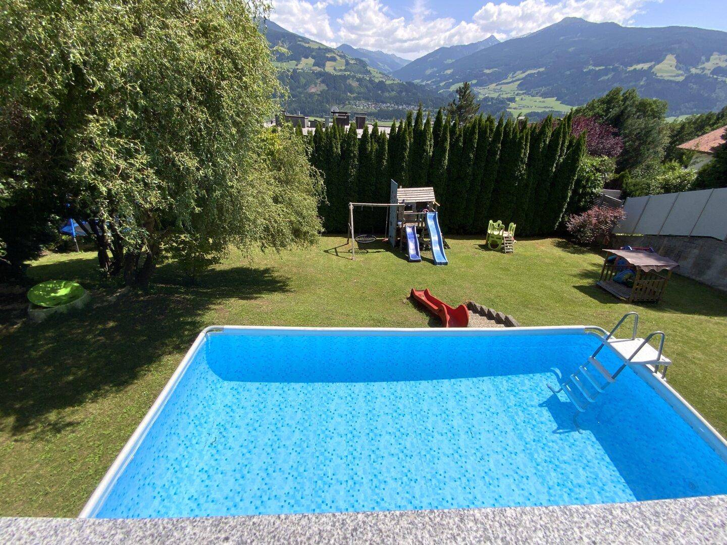 Weitläufiger Garten mit Aufstellpool, Kinderspielplatz und Blick auf die Berge.