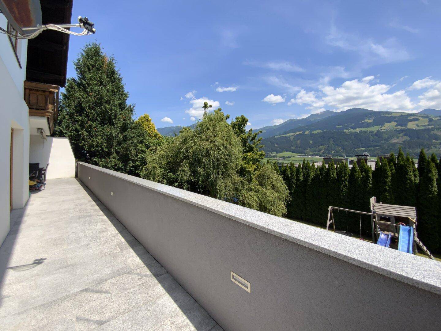 Langer Balkon mit Fliesenboden und weitem Blick auf die Berge und den Kinderspielplatz.