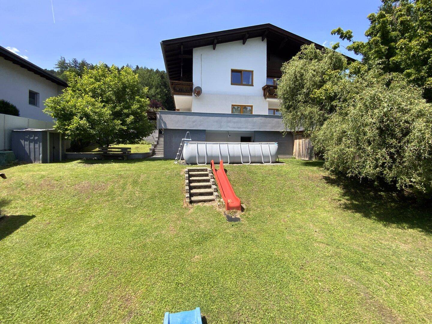 Großer Gartenbereich mit Rasenfläche, Aufstellpool und Kinderrutsche vor dem Haus.