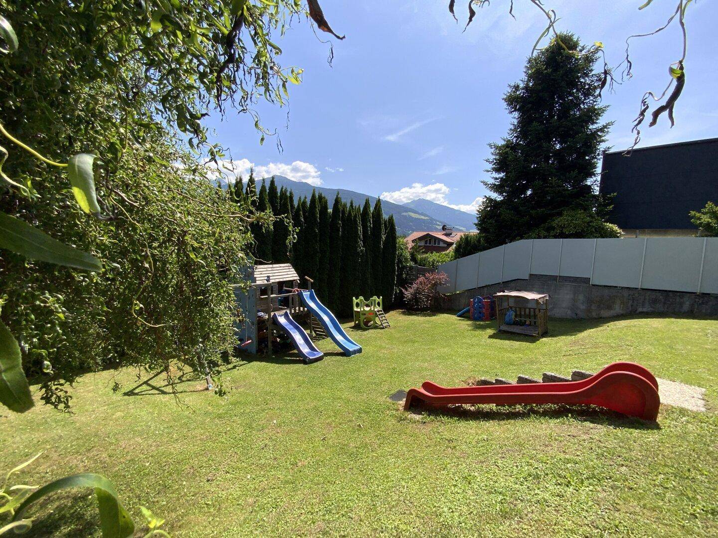Großer Garten mit Rasenfläche, Kinderspielplatz und hohen Hecken im Hintergrund.