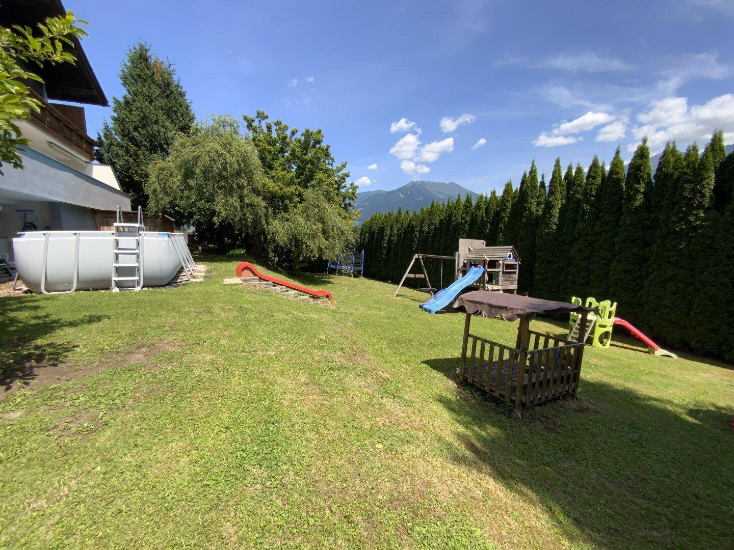 Weitläufiger Garten mit Aufstellpool, Kinderspielplatz und viel Grünfläche.