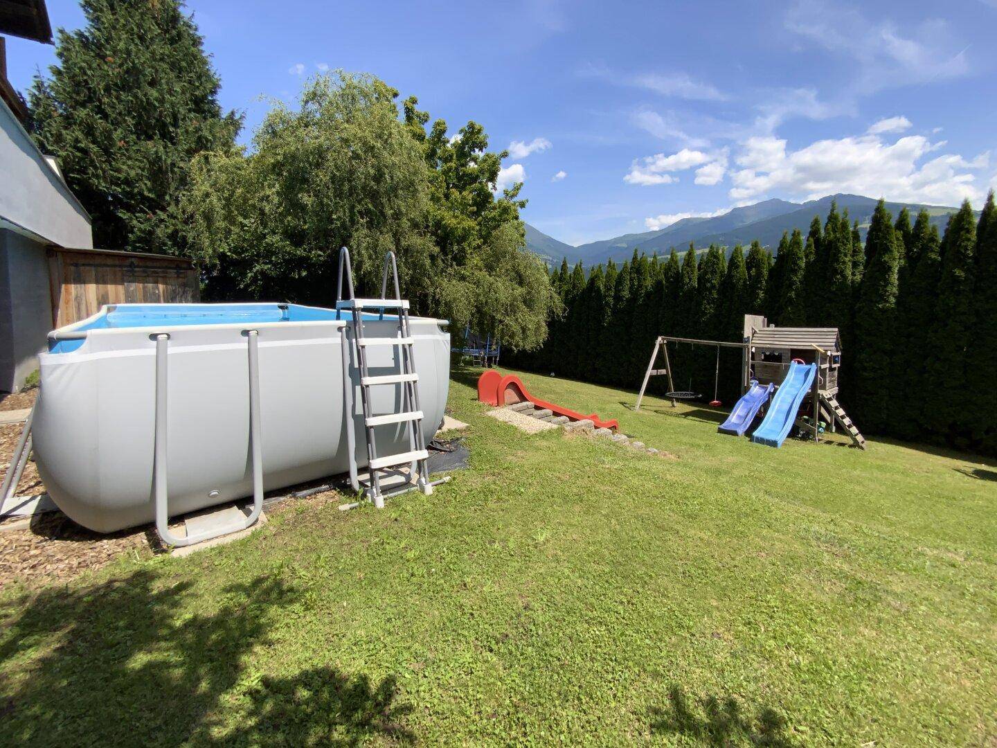 Geräumiger Garten mit Spielplatz, einem Aufstellpool und weitem Blick auf die umliegende Berglandschaft.