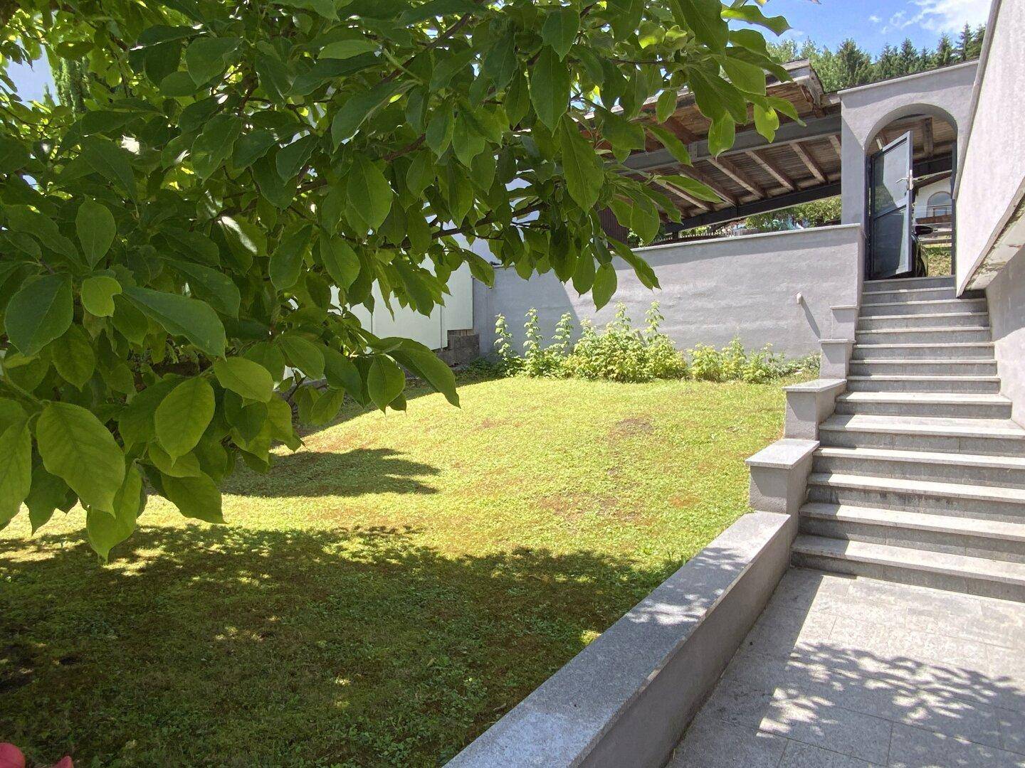 Grüner Gartenbereich mit Rasenfläche und Steintreppe, die zum Haus hinaufführt.