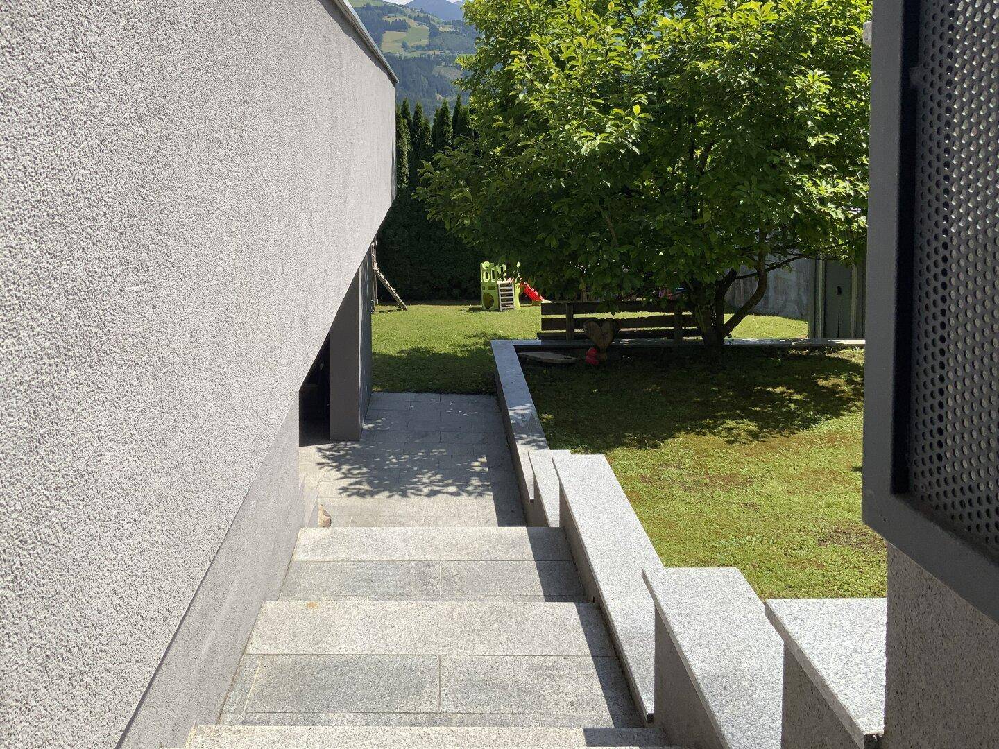 Außentreppe mit Granitstufen führt hinunter zum grünen Gartenbereich mit Rasen.