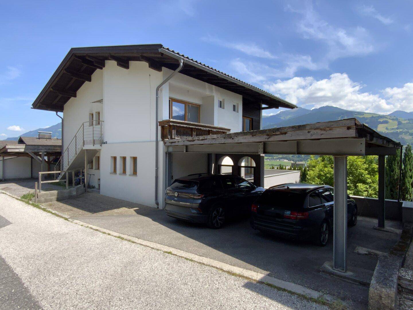 Ansicht des Hauses mit traditionellem Dach, Carport und Blick auf die Berglandschaft.