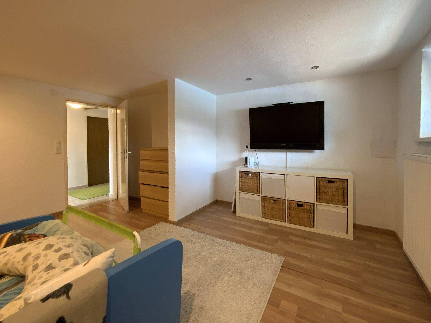 Kinderzimmer mit Laminatboden, Fernseher und Stauraum in einem hellen Ambiente.