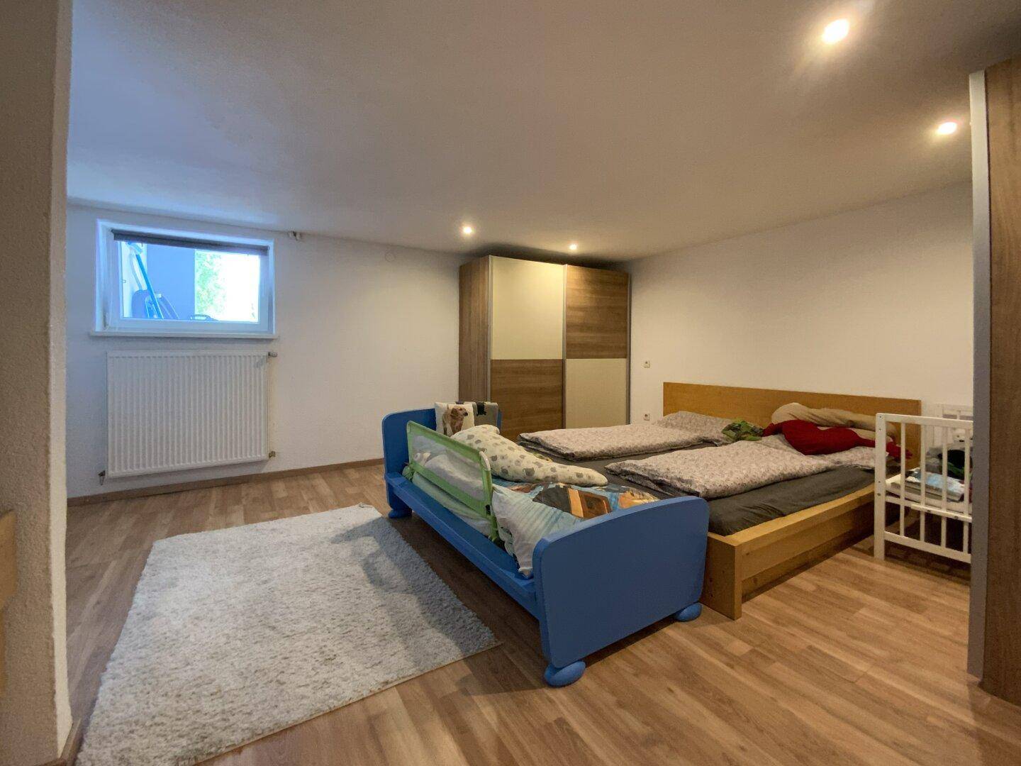 Helles Kinderzimmer mit Laminatboden, zwei Betten und einem Fenster.